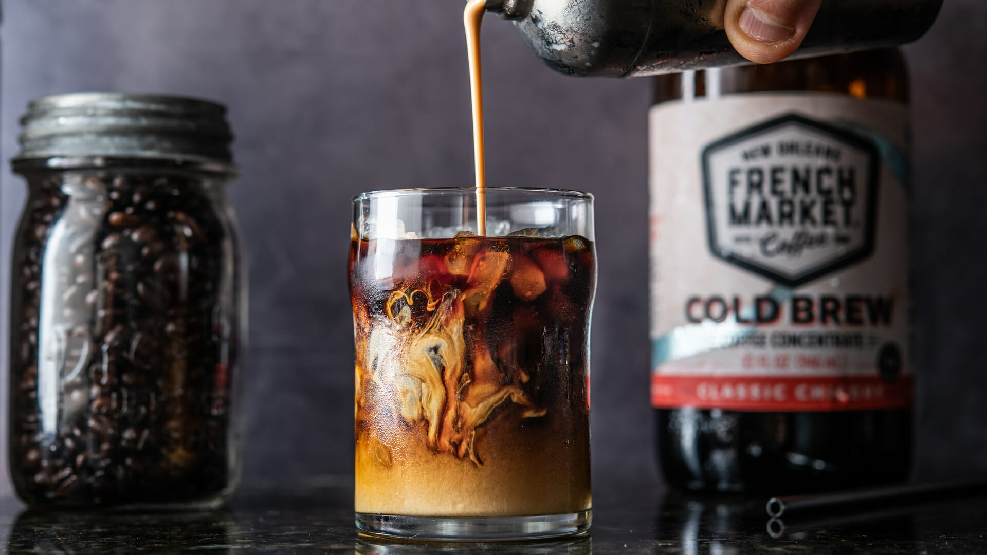 Milk being poured into a glass of French Market Vietnamese Iced Coffee on a dark kitchen counter