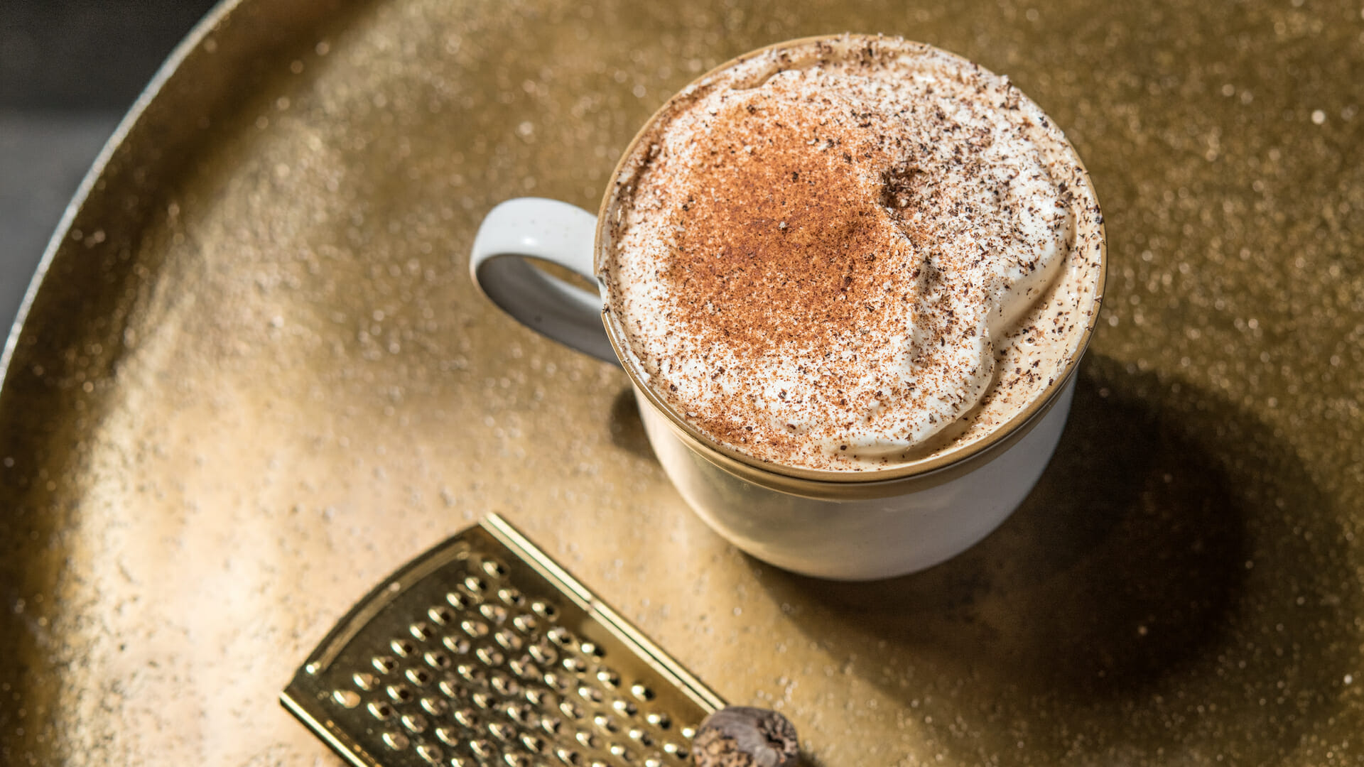 Overhead view of a French Market Spiced Latte with freshly grated nutmeg in a white coffee cup on a gold serving tray