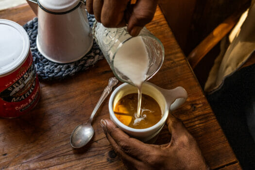 hand pouring hot milk into cup of coffee, making cafe au lait